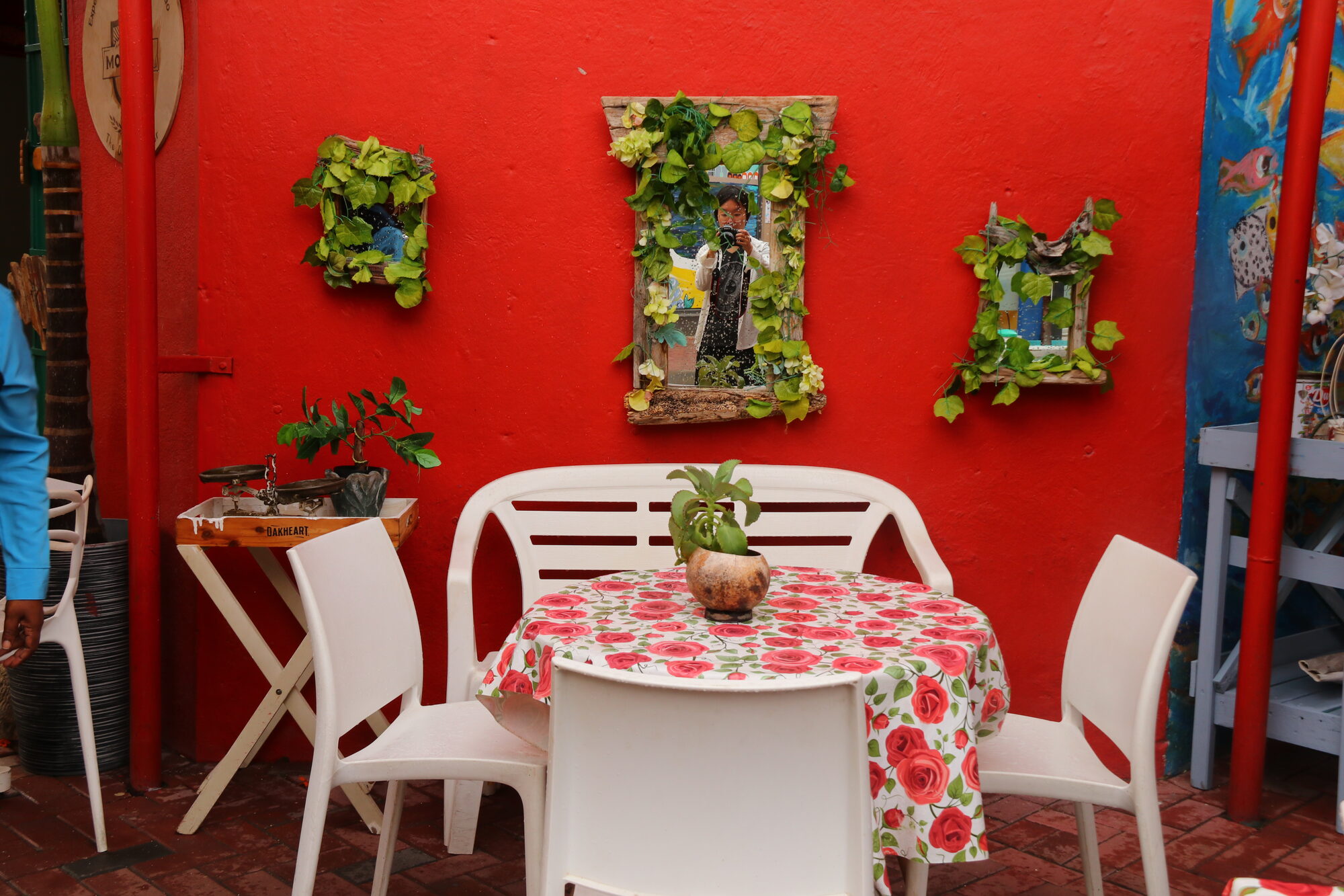 Bright red wall with plant art above a floral table and white chairs