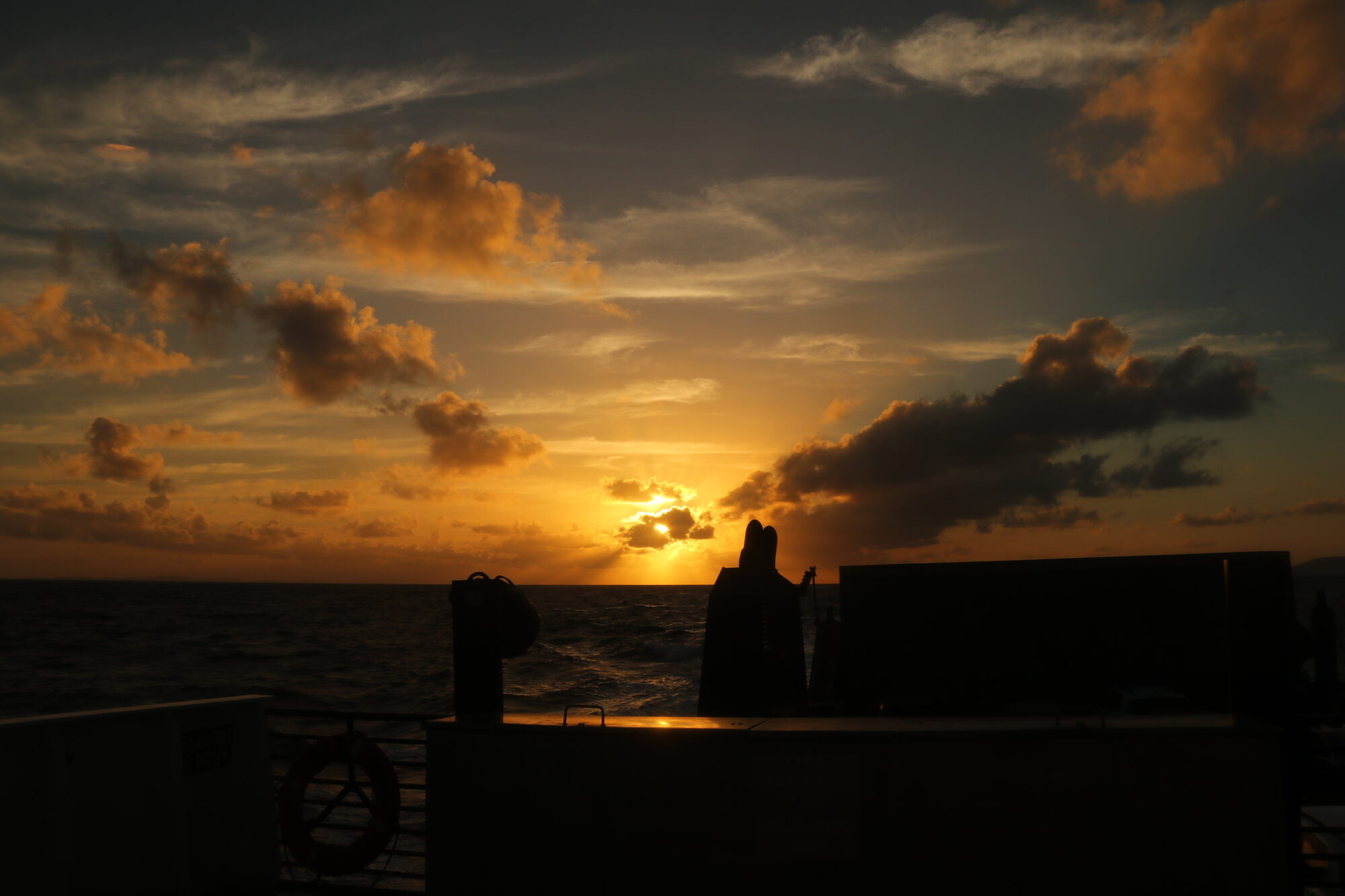 Sunset behind the darkened silhouette of the ship's deck
