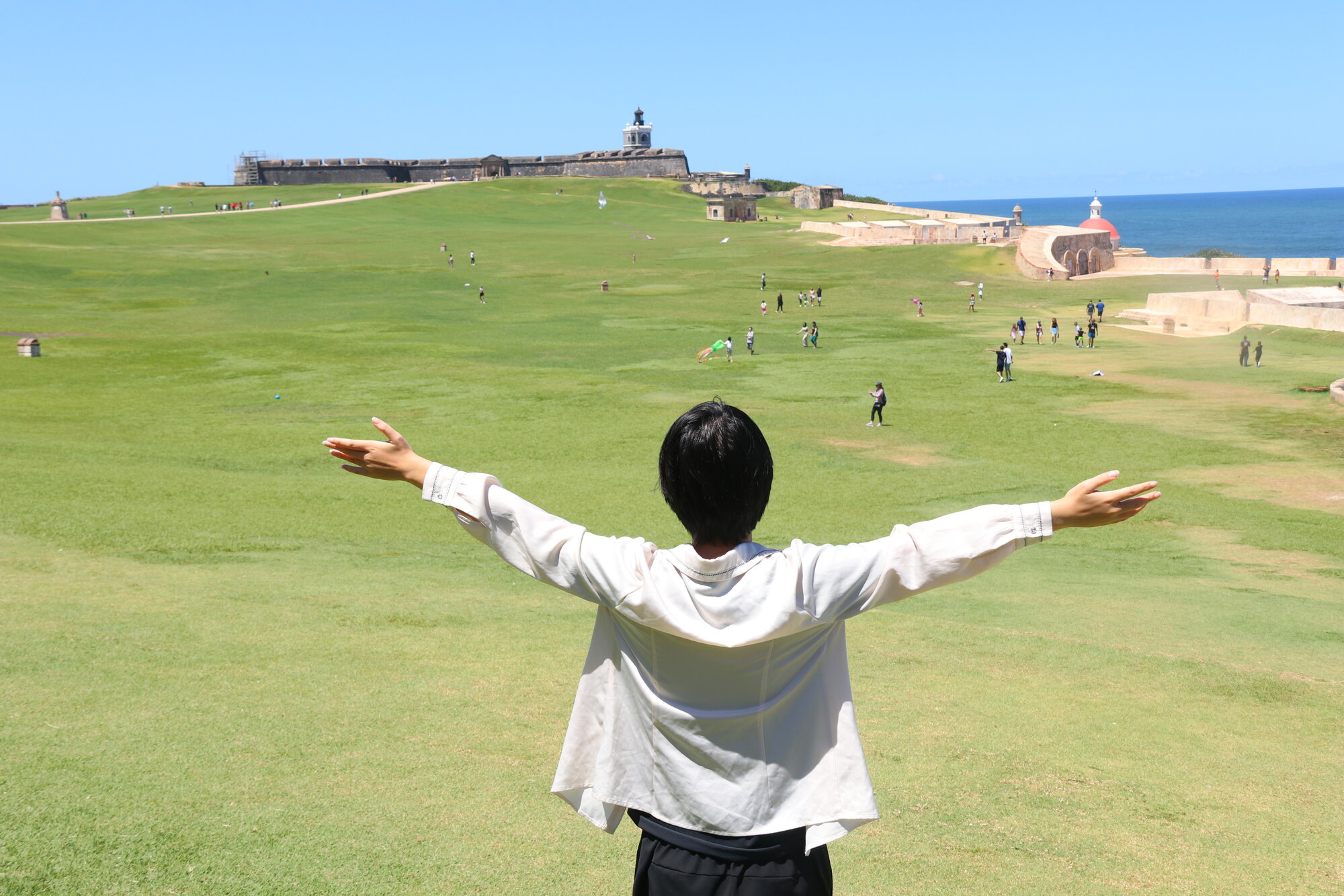 Arms outstretched on the lawn facing Castillo San Felipe del Morro